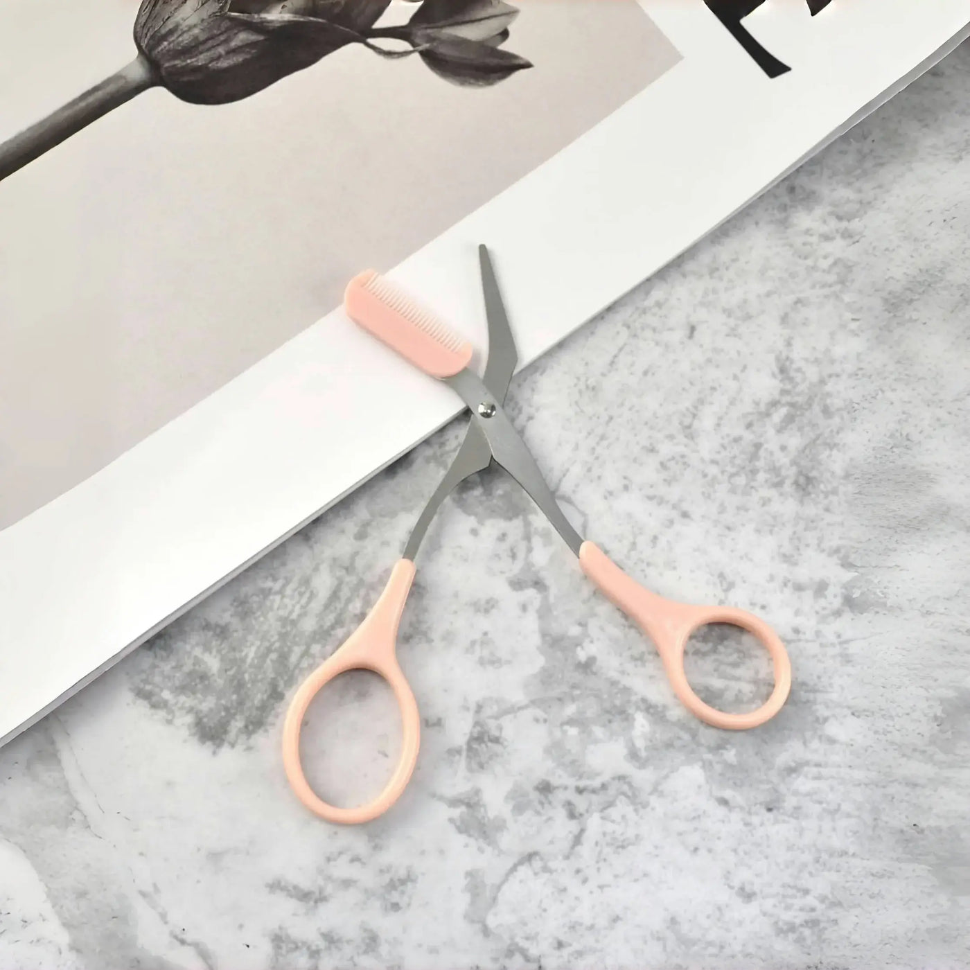 Frost Glow Cosmetics pink eyebrow scissors with built-in comb. Stainless steel, precise grooming tool for shaping perfect brows.