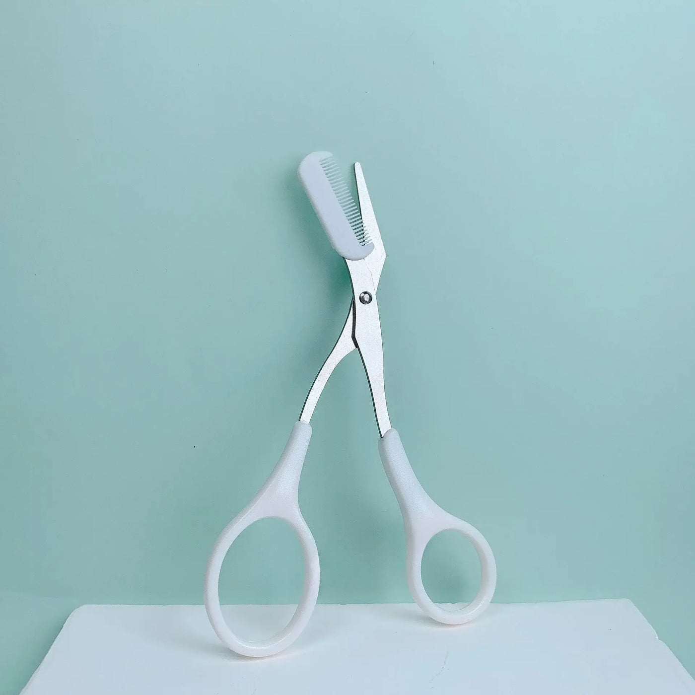 Frost Glow Cosmetics pink eyebrow scissors with built-in comb. Stainless steel, precise grooming tool for shaping perfect brows.