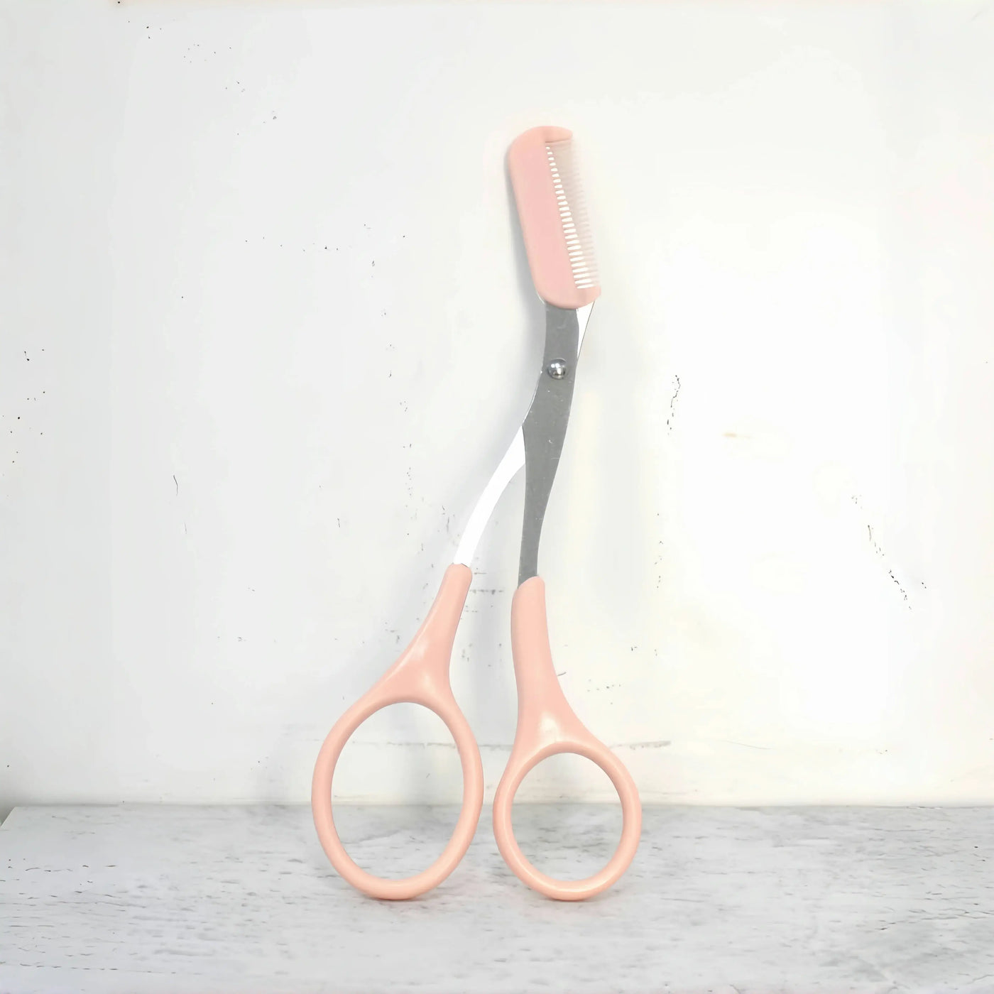 Frost Glow Cosmetics pink eyebrow scissors with built-in comb. Stainless steel, precise grooming tool for shaping perfect brows.