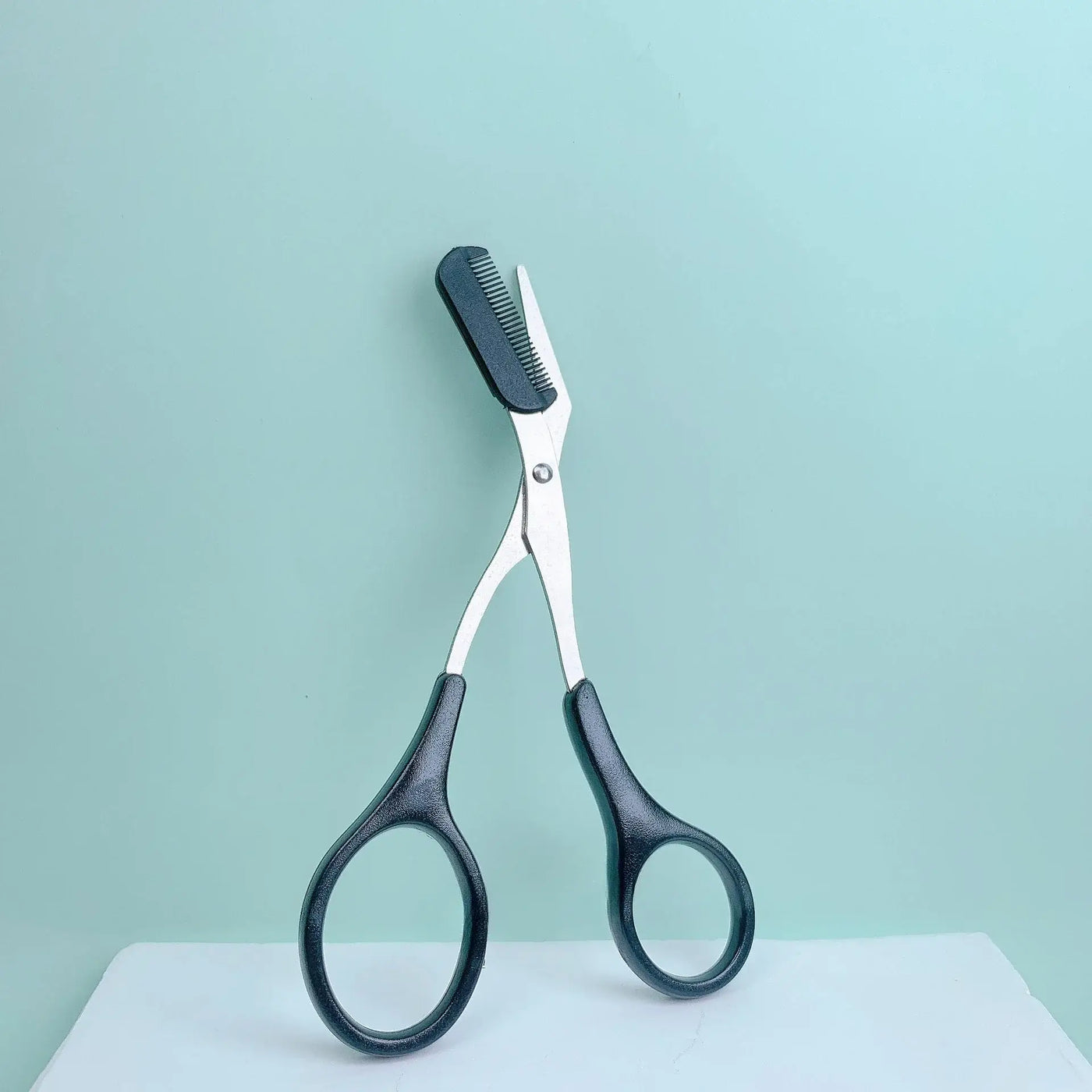 Frost Glow Cosmetics pink eyebrow scissors with built-in comb. Stainless steel, precise grooming tool for shaping perfect brows.